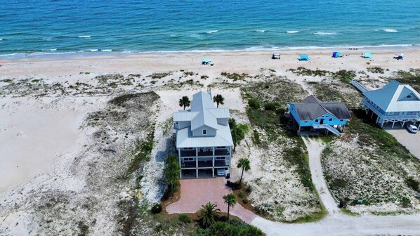 A beachfront property with a large house, a smaller building, and a beach area with umbrellas.
