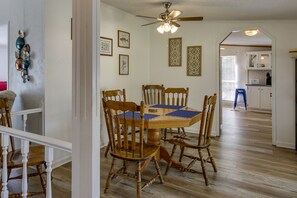 Zona pranzo con tavolo e sedie in legno, ventilatore a soffitto e cucina sullo sfondo.