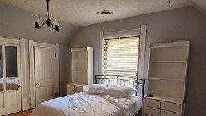 Ein Schlafzimmer mit einem Bett, einem Kleiderschrank, einem Nachttisch und einem Fenster mit Jalousien.