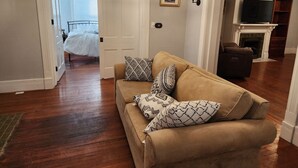 Ein Wohnzimmer mit einem beigen Sofa, gemusterten Kissen, einer Chandelierleuchtre, einem gerahmten Bild und einem Kamin.