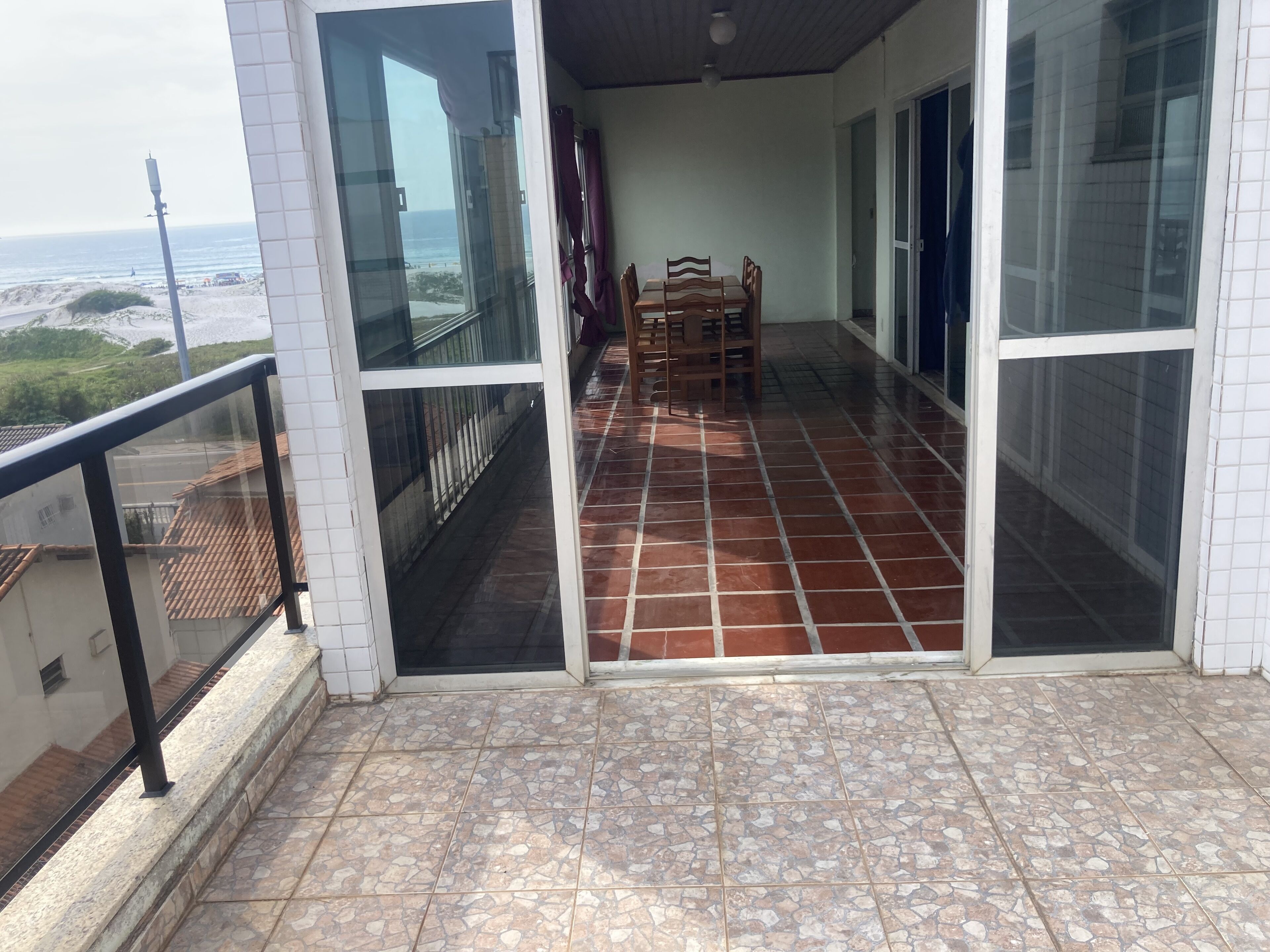 A balcony with a tiled floor, a table with chairs, and a view of the beach.