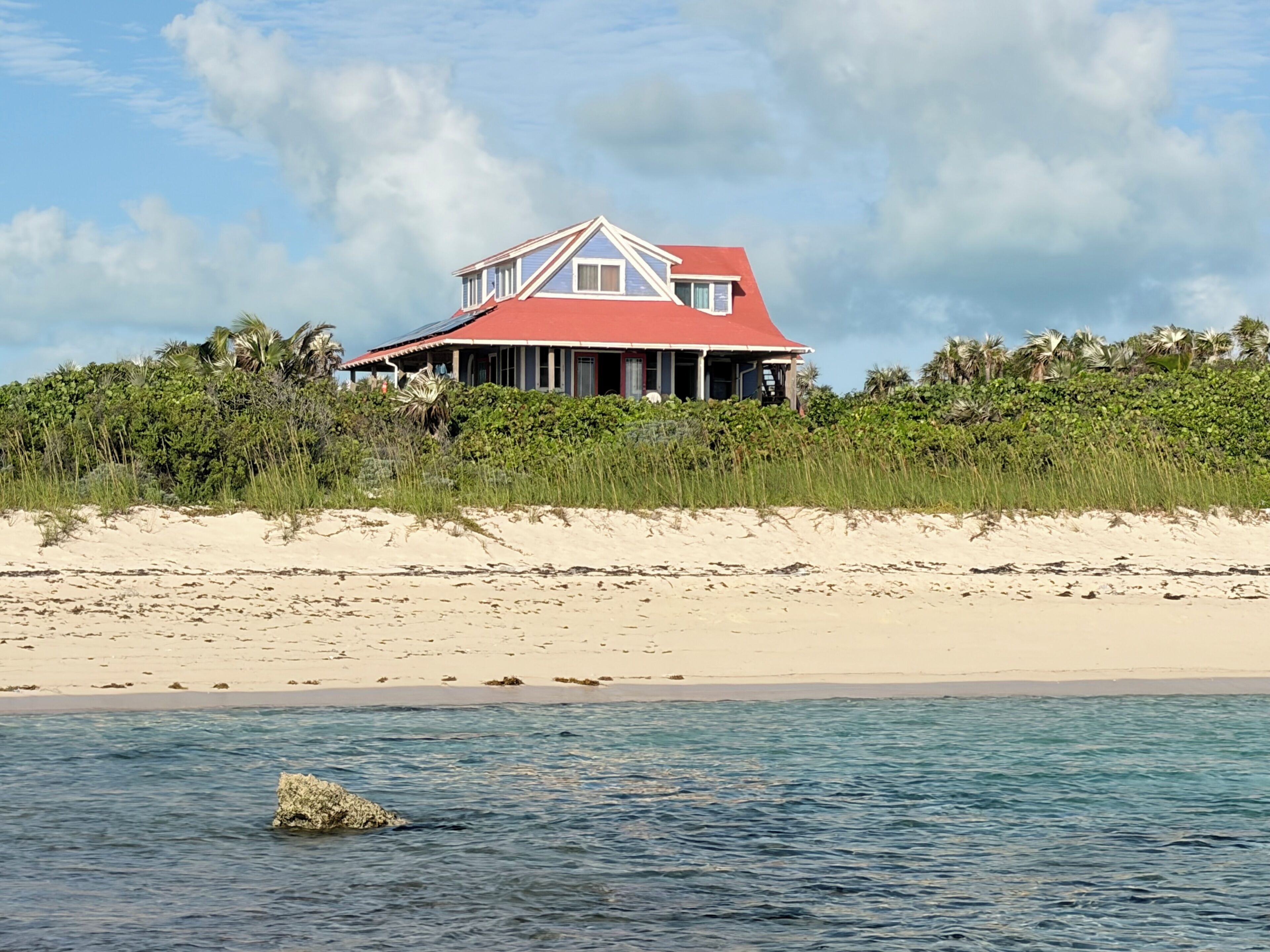 Una casa con tetto rosso affacciata su una spiaggia sabbiosa e vista sull'oceano.