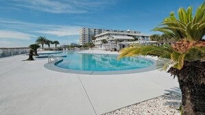 A swimming pool with a circular design, surrounded by a concrete deck. In the background, there is a multi-story building with balconies.