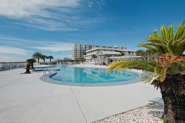 A swimming pool with a circular design, surrounded by a concrete deck. In the background, there is a multi-story building with balconies.