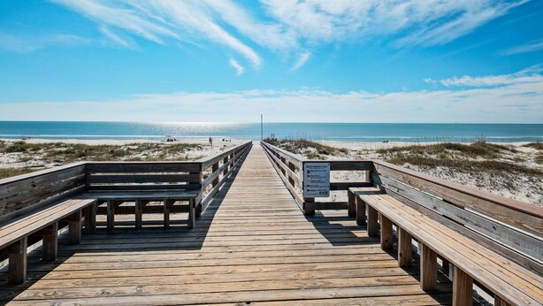 A wooden boardwalk leading to a beach with a sign warning of black sand.