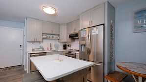 A modern kitchen with white cabinets, stainless steel appliances, a marble countertop, and a wooden bench.