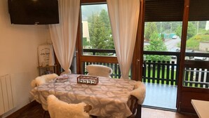 Ein gemütliches Zimmer mit einem Bett, einem Flachbildfernseher, einem Tisch mit einem Glasbehälter und Blick auf einen Balkon mit Geländer.