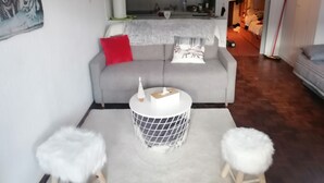 Ein modernes Wohnzimmer mit einem grauen Sofa, roten und weißen Kissen, einem kleinen runden Tisch mit einem weißen Korb und einem weißen, flauschigen Hocker.