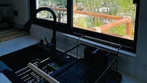 A room with a large window offering a view of a park and a distant body of water. - La Ventana Apartments Depa #4 (La Ventana)