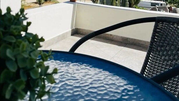 A balcony with a view of the ocean and cacti, featuring a wooden railing and a table with a chair. - La Ventana Apartments Depa #4 (La Ventana)