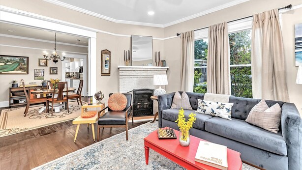 A living room with a grey sofa, red coffee table, and a fireplace. There is a dining area with a table and chairs in the background.