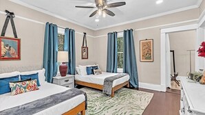 A bedroom with two beds, a ceiling fan, and a large window with curtains.