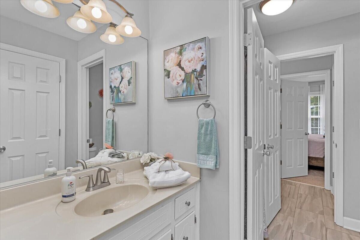 Une salle de bain avec un grand miroir, un lavabo et deux tableaux floraux encadrés accrochés au mur.