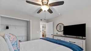 Ein Schlafzimmer mit einem Bett, einem Deckenventilator, einem Fernseher und einer Kommode.