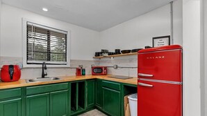 Cocina compacta con armarios verdes, un refrigerador rojo, un microondas y un lavamanos.