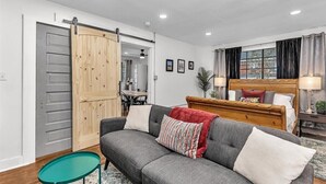 Una sala moderna con un sofá gris, puerta corredera de madera y una cama con cabecera.
