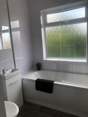 Bathroom features a bathtub, sink, and mirror, with a potted plant on the windowsill.