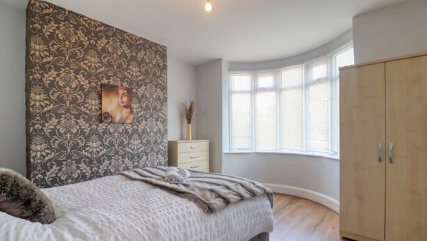 A bedroom with a large bed, a wardrobe, a nightstand, and a window with blinds. - Highfield House cosy 4 bedroom (Scunthorpe)