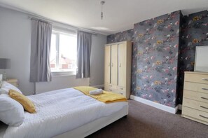 Relax in a cozy space with a neatly made bed, wardrobe, and dresser, surrounded by a floral patterned wall and carpeted floor.