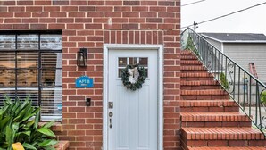 Une porte blanche ornée d’une guirlande, un bâtiment en briques et une enseigne bleue indiquant « APT B ».