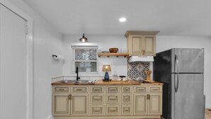 Une cuisine avec des meubles de couleur claire, un réfrigérateur en acier inoxydable, un plan de travail en bois et une fenêtre avec des stores.