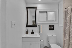 A bathroom with a white sink, a mirror, a toilet, and a shower curtain.