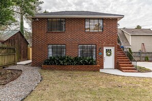 A two-story brick house with a front porch, a small garden, and a wooden fence.