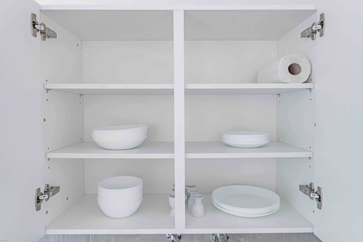Ein weißes Schränkchen mit vier Einlegeböden, auf denen weiße Schalen und Teller stehen.