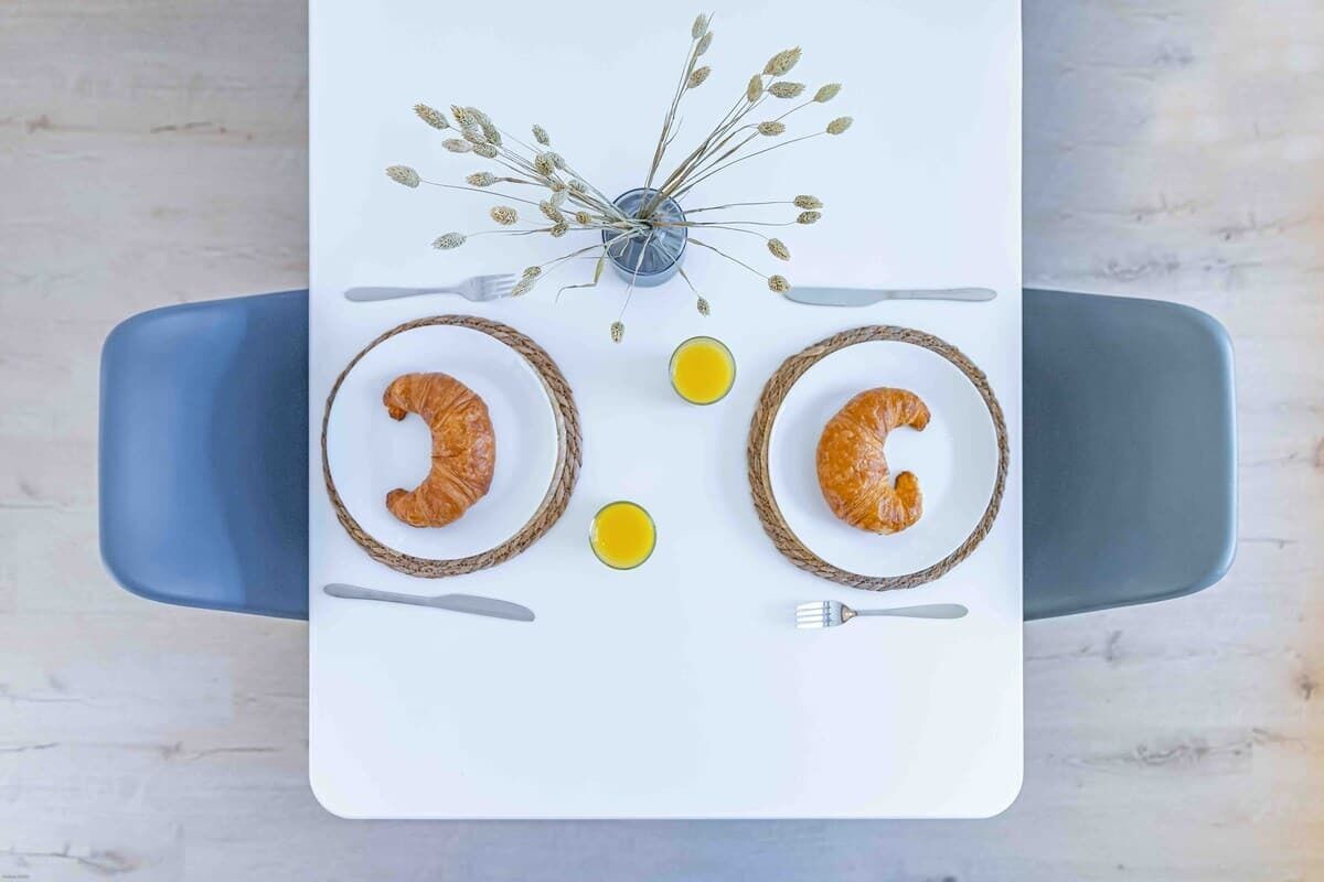 Ein Tisch mit zwei Tellern Croissants, einem Glas Saft und einer Vase mit getrockneten Blumen.