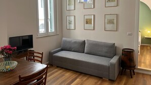 A living room with a grey sofa, wooden dining table, chairs, a TV, and framed artwork on the wall. - Apartment in the historic center of Rome (Roma)