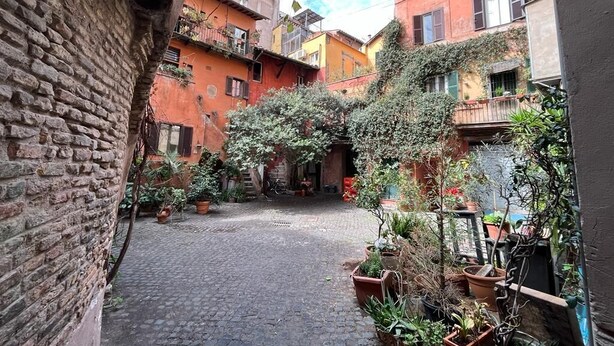 A narrow cobblestone alley with brick buildings on either side, potted plants, and a clear sky. - Apartment in the historic center of Rome (Roma)