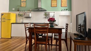 A compact kitchen with a dining area, featuring a yellow refrigerator, wooden chairs, a dining table, and a TV on a wooden stand. - Apartment in the historic center of Rome (Roma)