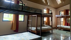 A dormitory room with bunk beds, a fan, and a window with curtains. - Arenal Family House (La Fortuna)