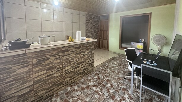 A kitchen with a tiled backsplash, a wooden countertop, a stove, and a sink. There is a dining area with a table and chairs. - Arenal Family House (La Fortuna)