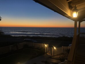A coastal view at dusk with a house overlooking the ocean, a porch with a railing, and a street lamp. - Casa De La Playa (La Jolla)