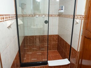 Zona de ducha con paredes de vidrio, azulejos marrones y blancos, una puerta negra y una toalla blanca en el suelo.