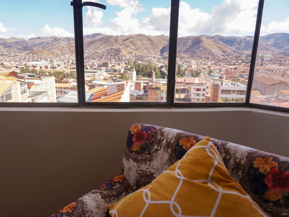 A room with a sofa and a window overlooking a cityscape with mountains in the background.