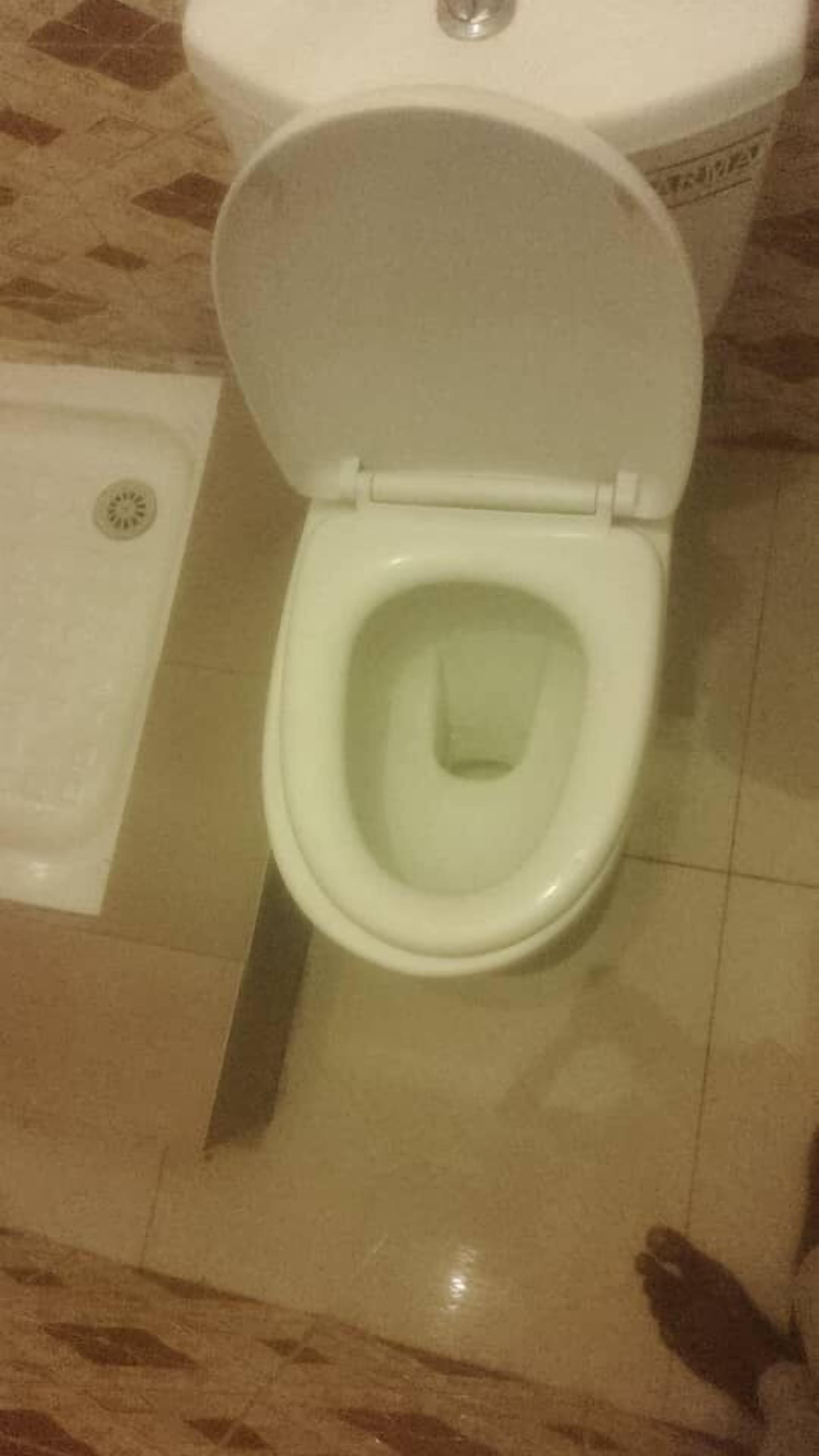 Een toilet met gesloten deksel, een zichtbare afvoer en een betegelde vloer.