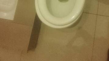 Een toilet met gesloten deksel, een zichtbare afvoer en een betegelde vloer.