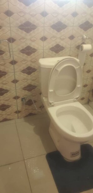 A toilet with a closed seat in a bathroom with patterned tiles. - Sharon Rose Hotel (Brazzaville)