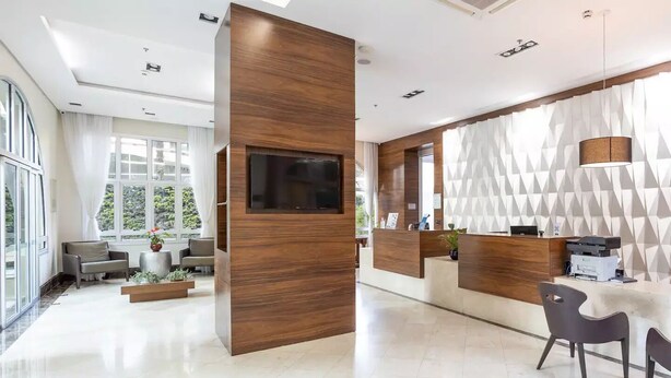 A modern hotel lobby with a reception desk, seating area, and a large TV screen.