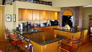 A spacious kitchen with wooden cabinets, a central island with bar stools, a brick oven, and various appliances. - Hanging H Lodge (Sutherland)