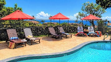 A poolside area with lounge chairs, red umbrellas, and a sign reading 'ALOHA HAWAII'.
