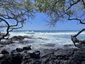 A rocky shoreline with waves crashing against the rocks under a clear blue sky.