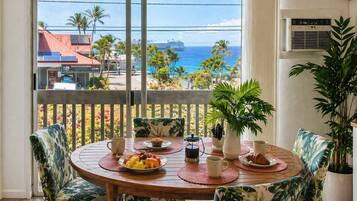 A round table with a view of the ocean, surrounded by chairs with tropical leaf patterns.