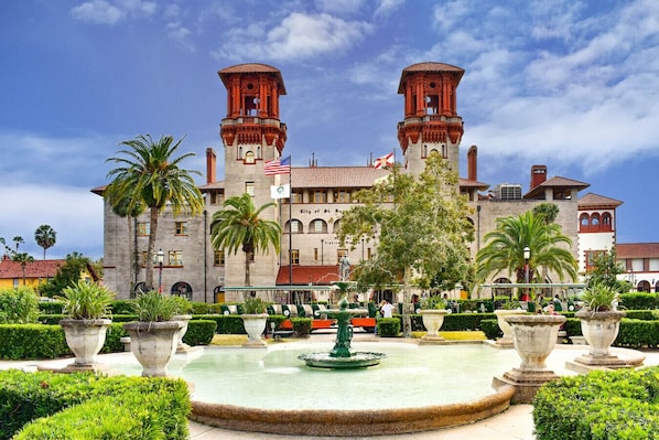 A historic building with two towers, a fountain, and well-maintained gardens.