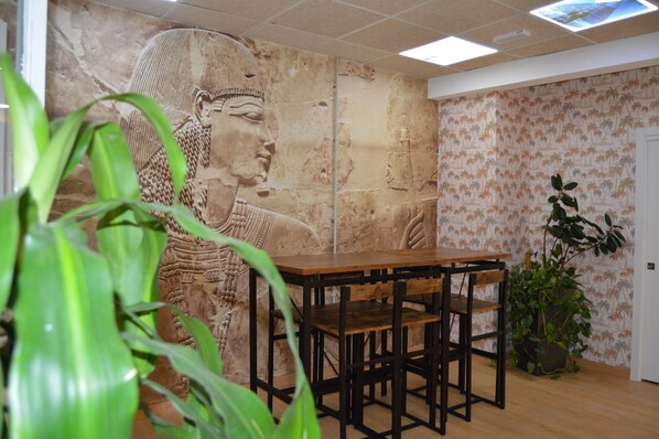 Una habitación con un mural grande, una mesa de madera, sillas y plantas en macetas.