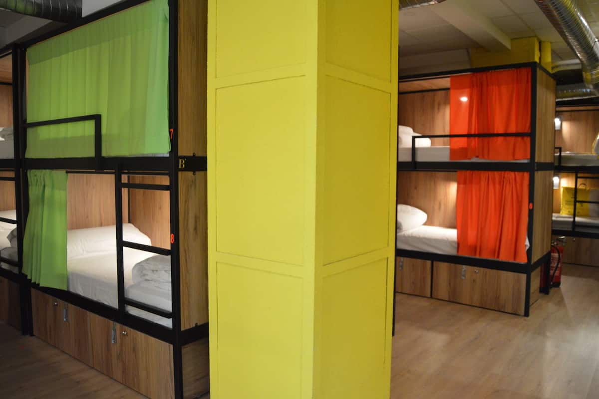 A hotel room with bunk beds, wooden flooring, and a yellow pillar.