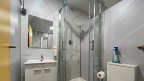 A bathroom with a glass-enclosed shower, a white sink, and a toilet. - DEBOD HOSTEL (Madrid)