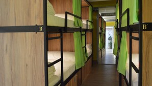 A corridor with bunk beds, each with a green curtain. - DEBOD HOSTEL (Madrid)